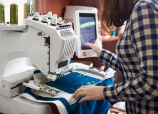 Close-up of woman working on modern computerized embroidery machine creating green floral pattern.