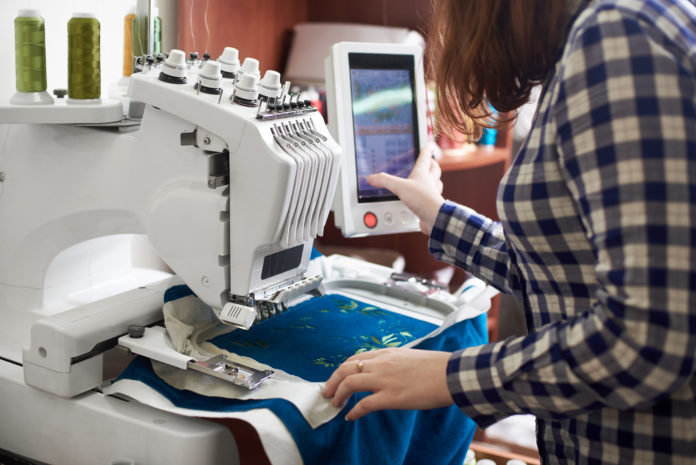 Close-up of woman working on modern computerized embroidery machine creating green floral pattern.